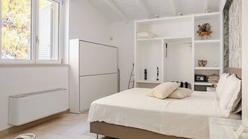 Un dormitorio con cama, armario, radiador y ventana con vista a árboles.