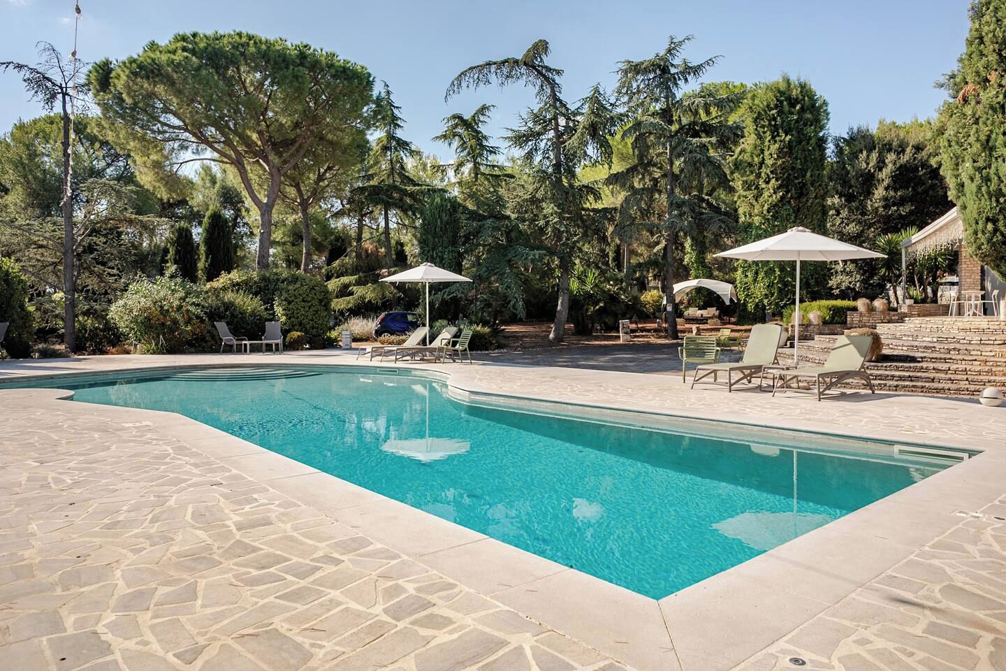 Una piscina rectangular con solárium de losas de piedra, rodeada de sillones de playa y sombrillas.