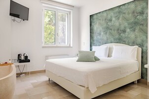 Ein Schlafzimmer mit einem Bett, einem Fenster, einem an der Wand befestigten Fernseher und einer Kaffeemaschine auf einer Ablagefläche.