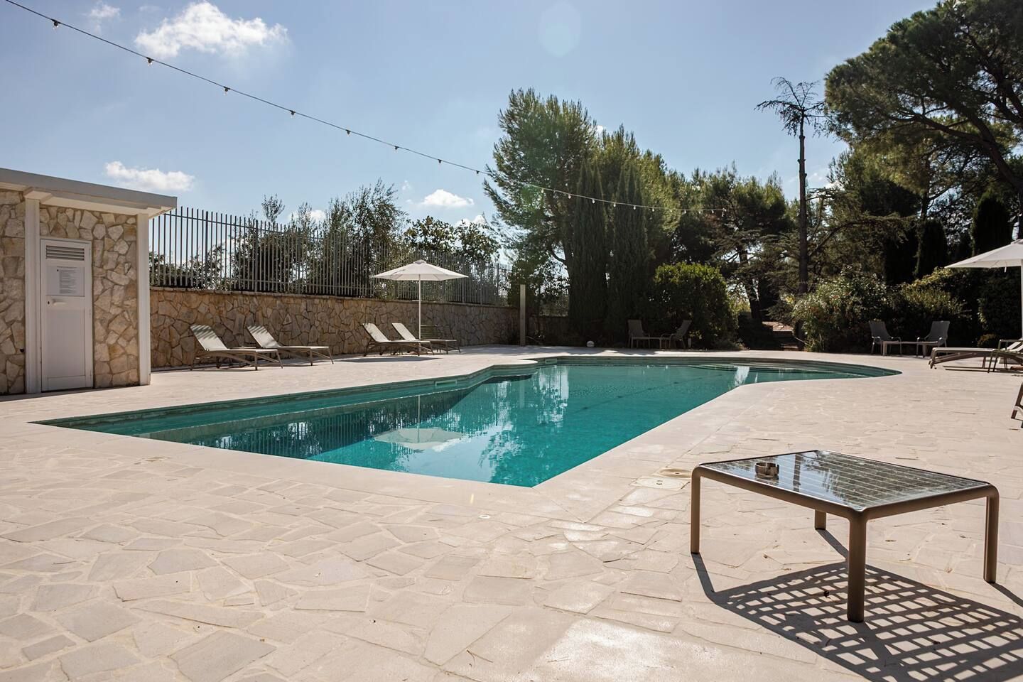 A swimming pool with lounge chairs and umbrellas, surrounded by stone walls and trees.
