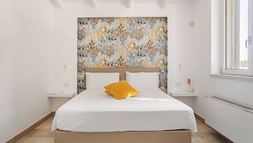 A bedroom with a large bed, a headboard with a floral pattern, a window, and a radiator.