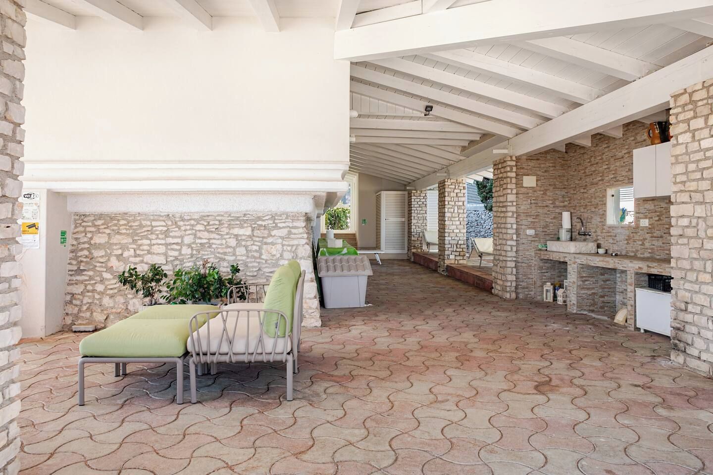 A covered outdoor area with a stone fireplace, seating, and a kitchen area.