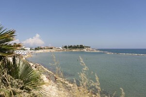 Escena de playa costera con cielos despejados, orilla arenosa y mar tranquilo.