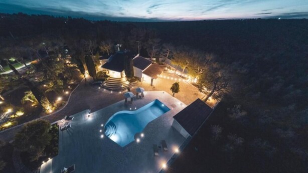 An aerial view of a property with a swimming pool, outdoor seating, and a well-lit patio area.