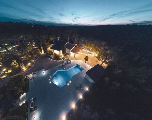 An aerial view of a property with a swimming pool, outdoor seating, and a well-lit patio area.