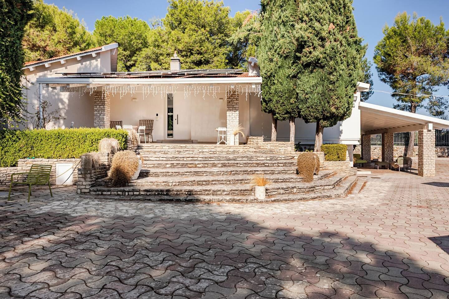 A house with a stone staircase leading to a front door, a covered patio area, and a well-maintained garden with hedges and shrubs.