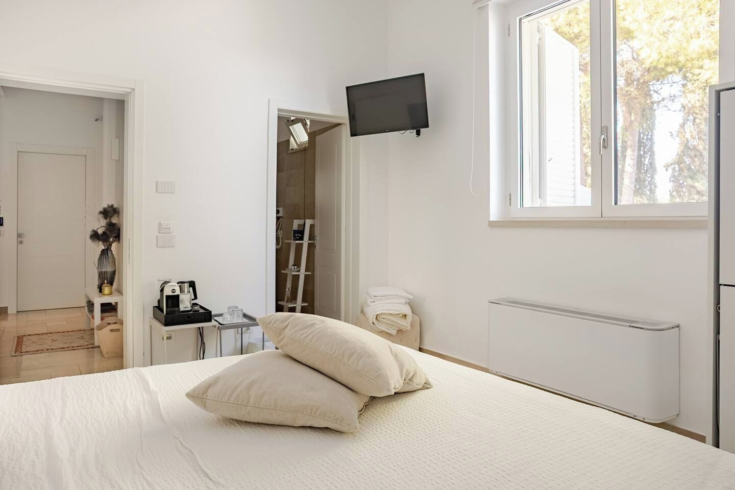 Une chambre d’hôtel avec un lit, un téléviseur fixé au mur, une fenêtre et une salle de bain visible à travers une porte ouverte.