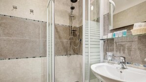 Une salle de bain moderne avec une douche à parois de verre, un lavabo blanc et un mur recouvert de carreaux.