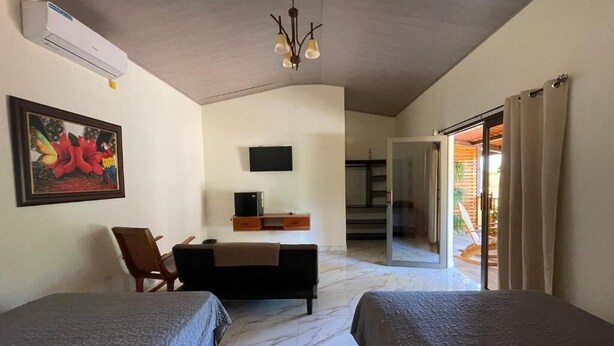 A hotel room with two beds, a desk, a chair, a TV, and a sliding glass door leading to an outdoor area.