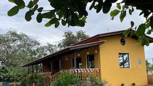 A yellow building with a porch, a staircase, and a small garden area with plants and a gravel path.