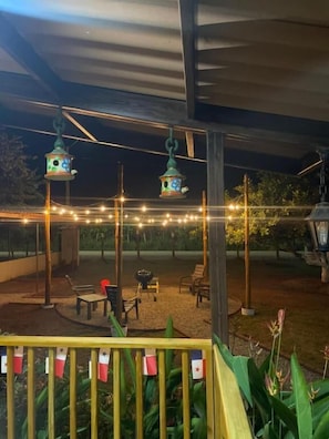 An outdoor patio area with string lights, hanging birdhouses, and a wooden fence with flags.