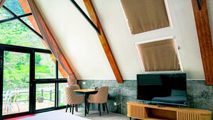 A modern room with a large bed, a TV, and a dining area with chairs. - Roameo Resorts (Sharda)