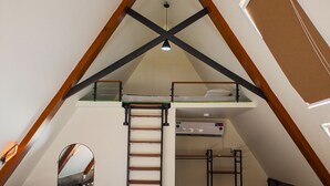 A bedroom with a loft bed, a ladder, a mirror, and a small desk area. - Roameo Resorts (Sharda)