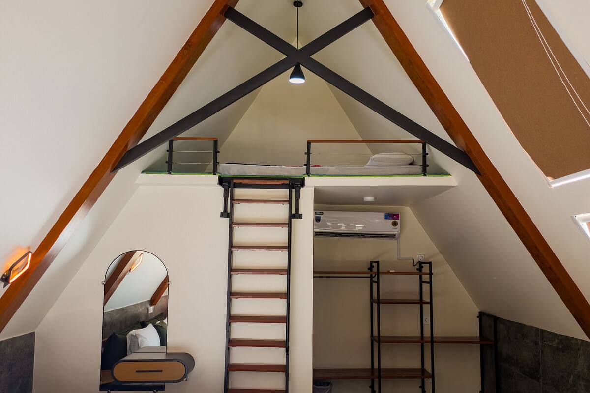 A bedroom with a loft bed, a ladder, a mirror, and a small desk area.