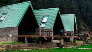 A building with a green roof, multiple windows, and a view of a forested mountain range. - Roameo Resorts (Sharda)