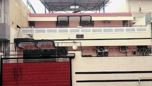 Un edificio de dos pisos con una puerta de garaje roja, un balcón con barandilla metálica y un letrero sobre la puerta.