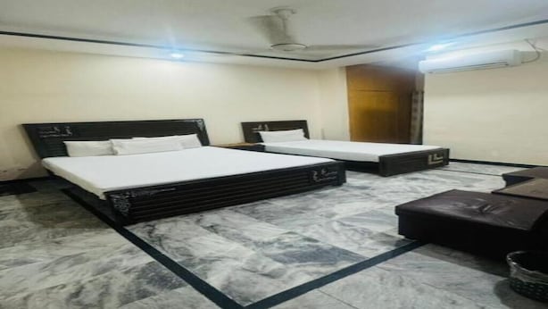 Habitación de hotel con dos camas, piso de mármol, ventilador de techo y aire acondicionado instalado en la pared.