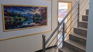 Una escalera con barandilla de metal, un cuadro grande enmarco de un paisaje, y vista de un edificio a través de una puerta abierta.
