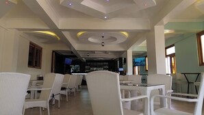 A restaurant with white wicker furniture, a bar area, and a television screen. - The Africana Hotel- Isiolo (Isiolo)