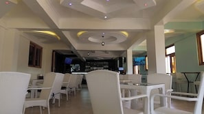 A restaurant with white wicker furniture, a bar area, and a television screen. - The Africana Hotel- Isiolo (Isiolo)