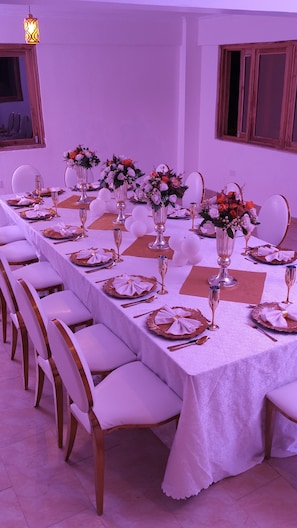 Ein langer Esstisch, gedeckt mit weißen Tischdecken, Besteck und floralen Tischdekorationen.