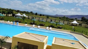 A swimming pool with lounge chairs and umbrellas, surrounded by a landscaped area with a view of distant hills. - The Africana Hotel- Isiolo (Isiolo)