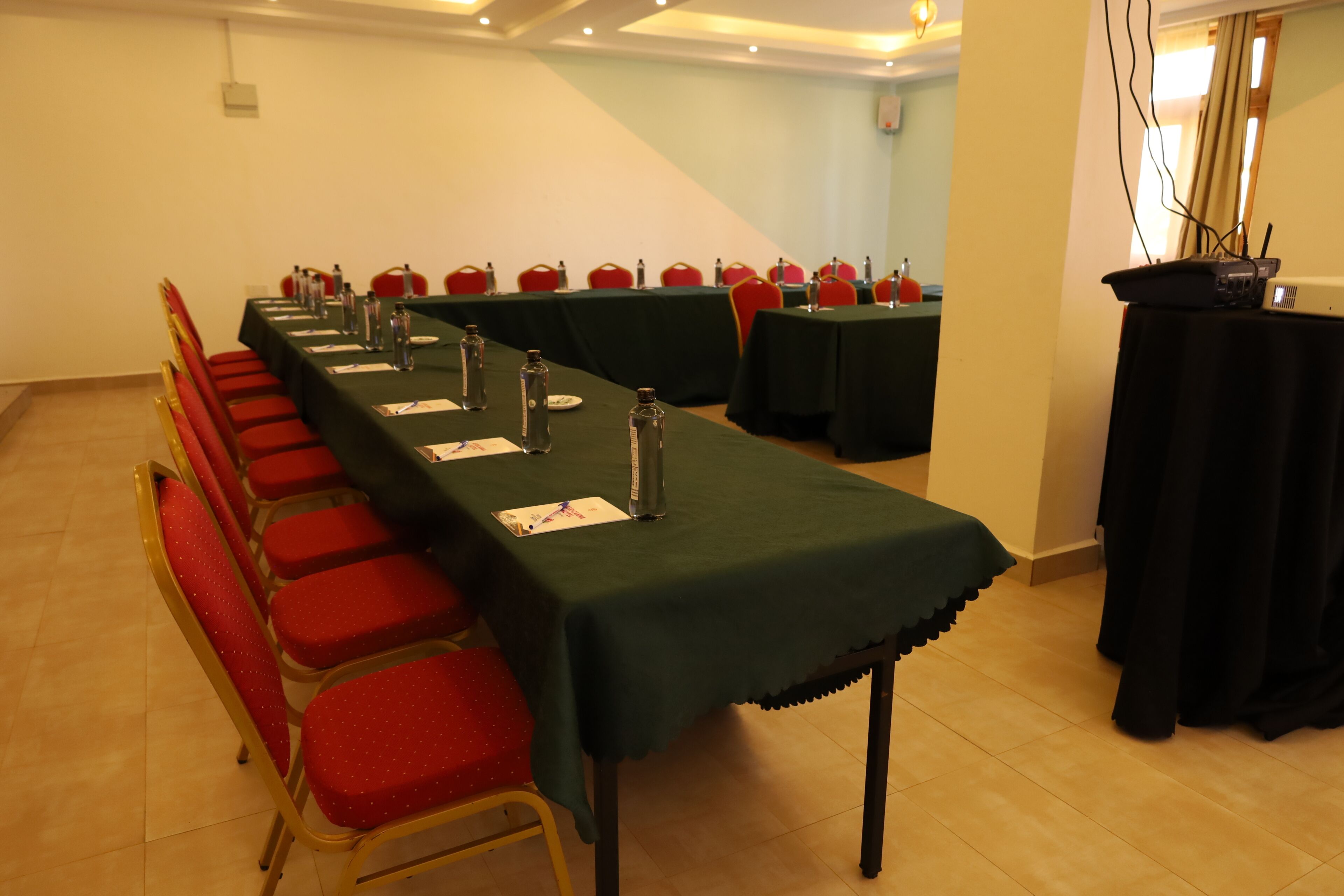 Un salón de conferencias con una larga mesa, sillas rojas y un proyector sobre un atril.