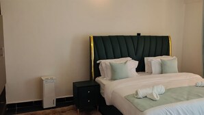 A hotel room with a bed, pillows, a bedside table, a heater, and a window with curtains. - The Africana Hotel- Isiolo (Isiolo)