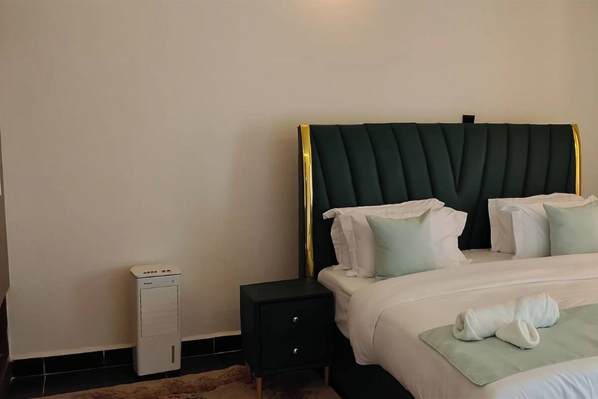 Ein Hotelzimmer mit Bett, Kissen, Nachttisch, Heizung und einem Fenster mit Vorhängen.