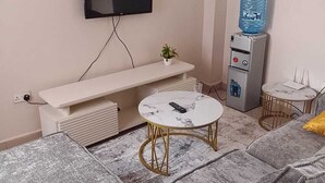 Una sala de estar moderna con sofá, una mesita redonda, televisor montado, dispensador de agua y radiador.