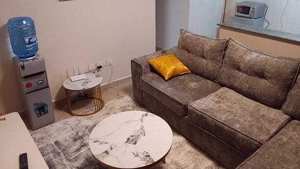 Sala de estar con sofá, una mesita de centro, dispensador de agua, una pequeña mesa y una obra de arte colgada.