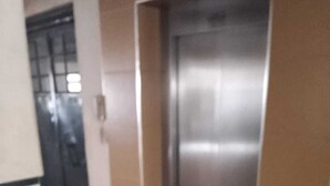 Un pasillo con un ascensor metálico, una puerta con ventanal y suelo alfombrado.