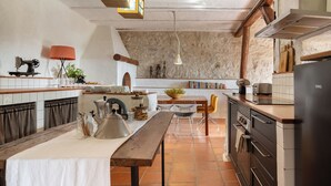 Une cuisine avec une table en bois, des luminaires suspendus et un mur recouvert de carreaux.