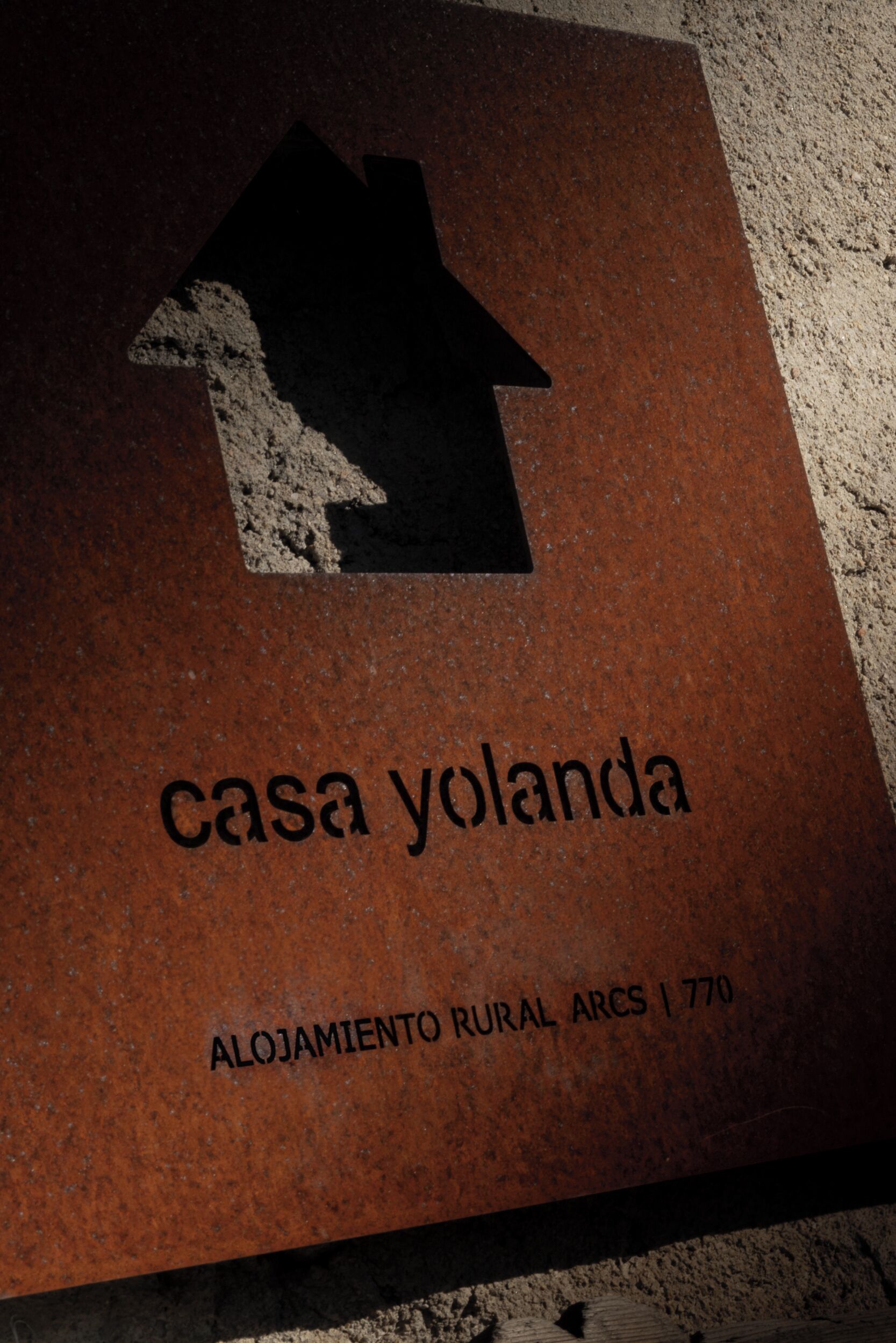 A sign with a house symbol and the text 'casa yolanda' and 'Alojamiento Rural Arcs | 1770'.