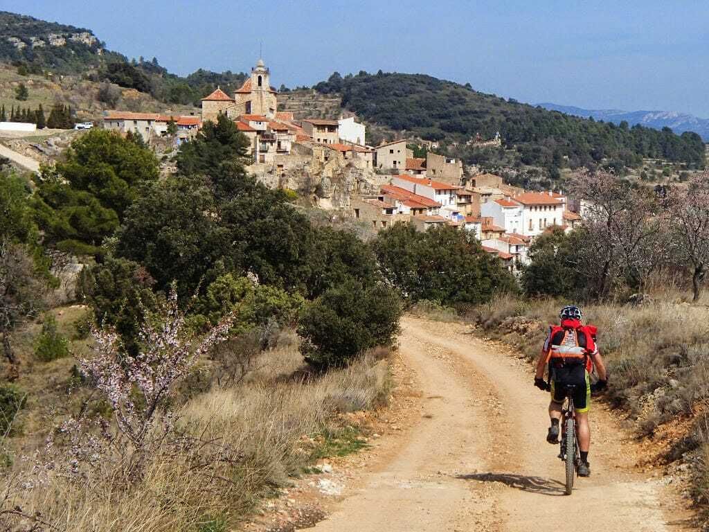 Un ciclista en un sendero de tierra con un pueblo al fondo.
