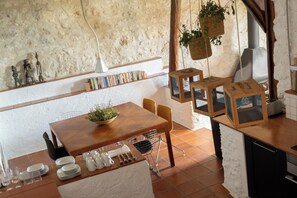 A rustic kitchen with a wooden table, hanging plants, and a stone wall.