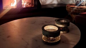 Une pièce aux murs de pierre, dotée d’un poêle à bois, d’un téléviseur à écran plat fixé au mur et d’une table ronde sur laquelle reposent deux objets ressemblant à des bougies.