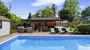 Un jardin avec une piscine, un espace salon extérieur et une terrasse couverte.