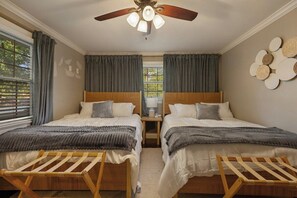 A bedroom with two beds, a ceiling fan, a window with curtains, and a wall decoration.