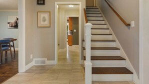 Un escalier menant à un deuxième étage, une œuvre d’art encadrée accrochée au mur et un coin repas avec des chaises et une table.