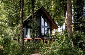 Eine moderne Holzhütte mitten im Wald, mit großen Fenstern und einer Holzterrasse.