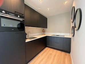 Eine moderne Küche mit dunklen Schränken, einem eingebauten Backofen und Holzboden.