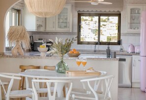 A kitchen with a round dining table, chairs, a vase with flowers, and two glasses of orange juice. - Villa COSTA AZZURRA by Abahana Villas (Benissa)
