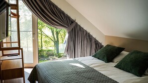 Una camera da letto con un letto, cuscini, una scala in legno e vista sugli alberi attraverso una finestra.