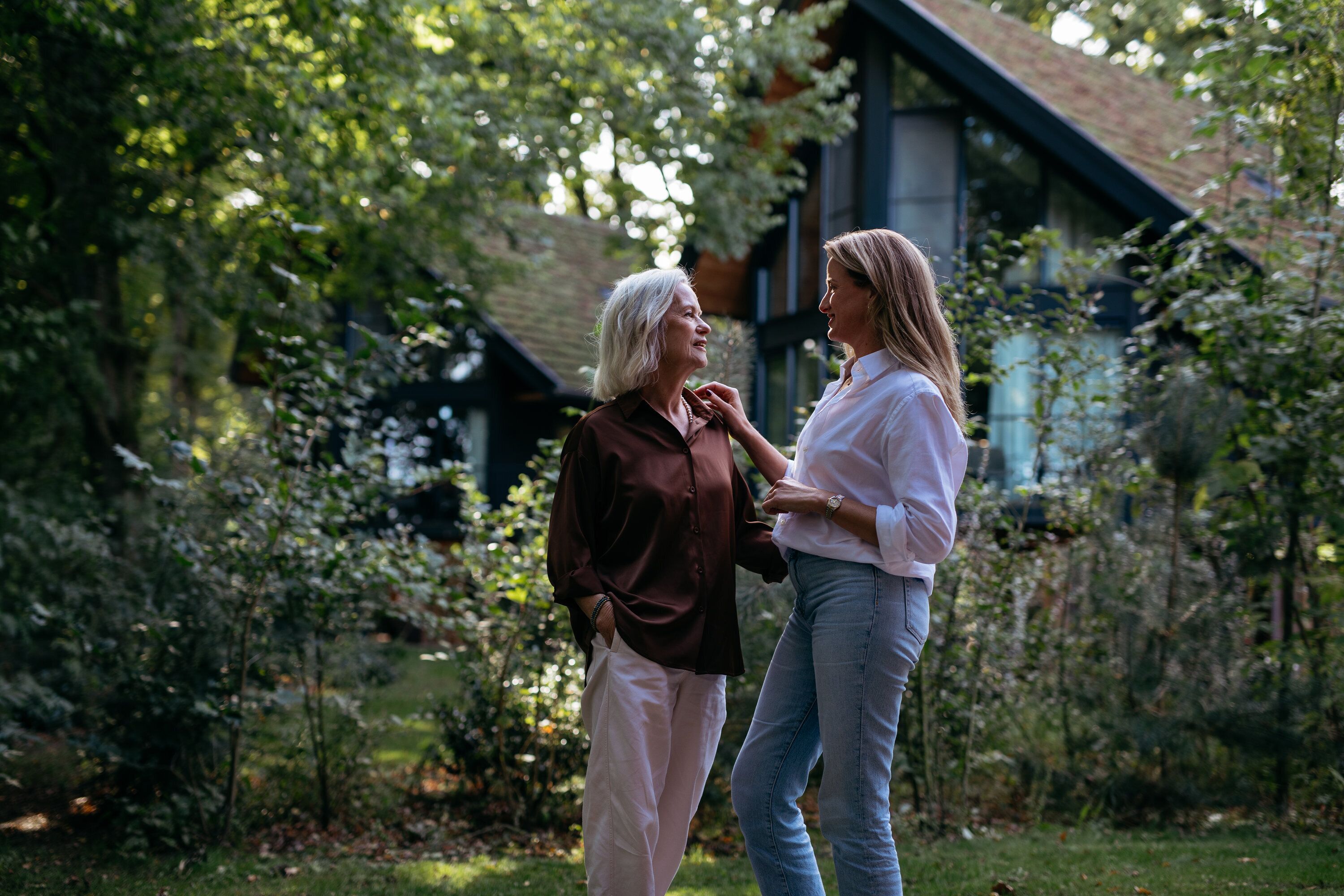 Two individuals standing in a garden with a building in the background.