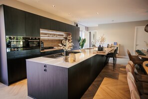 Une cuisine moderne avec des meubles de couleur sombre, une hotte en acier inoxydable et un îlot central doté d’un plan de travail en verre.