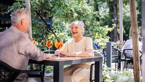 Dos personas sentadas en una mesa al aire libre con bebidas, rodeadas de follaje.
