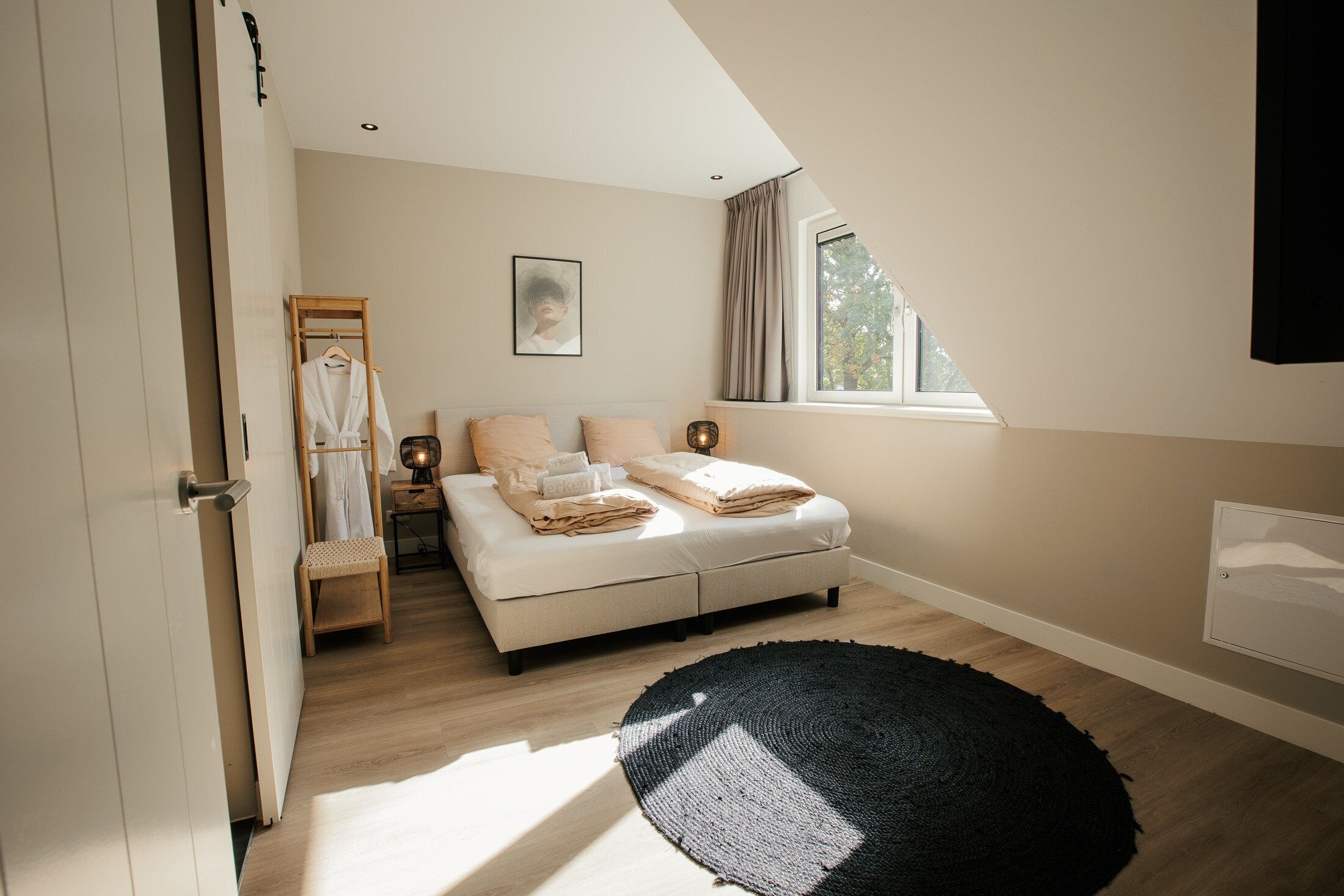 Ein Schlafzimmer mit einem Bett, Nachttischlampen, einem Fenster mit Vorhängen, einer Holzleiter und einem schwarzen Teppich.