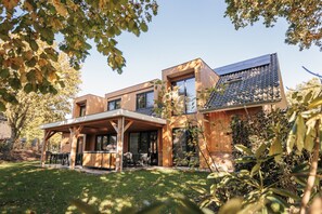 Une maison moderne à deux étages, dotée d’un patio couvert et d’un grand barbecue.