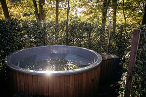 Ein hölzernes Whirlpool im Garten, umgeben von Bäumen und einer Hecke.
